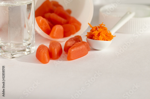 orange gummy vitamins like carrots (carotene supplement) on white background, copy space photo