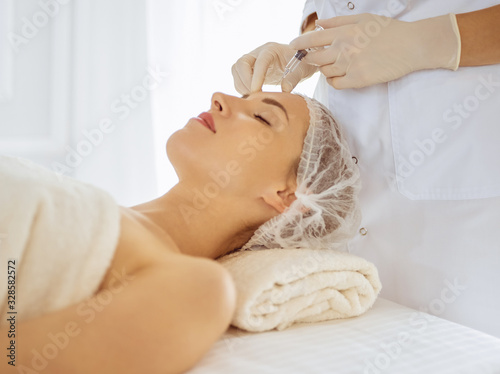 Beautiful woman receiving beauty injections with closed eyes. Beautician doctor hands doing beauty procedure to female face with syringe. Cosmetic medicine and surgery concept