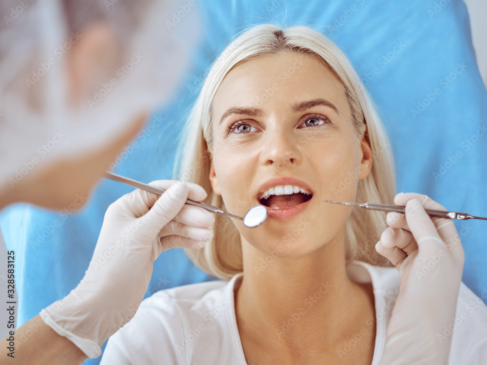 Smiling blonde woman examined by dentist at dental clinic. Healthy teeth and medicine concept Smiling blonde woman examined by dentist at dental clinic. Healthy teeth and medicine concept