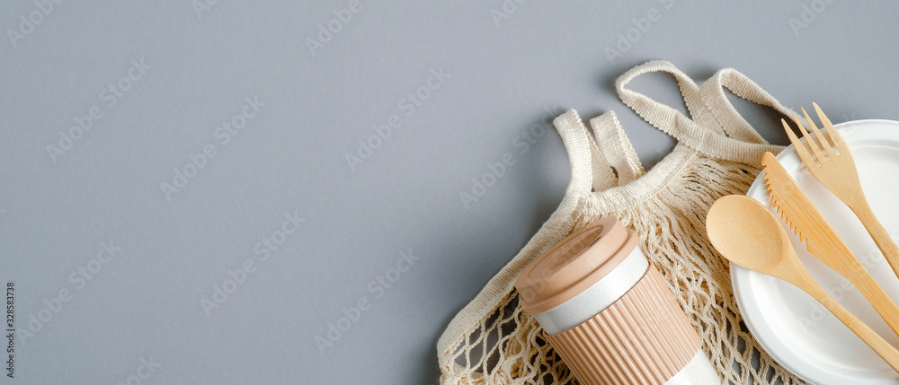 Reusable mesh bag with eco-friendly wooden cutlery and bamboo coffee cup on grey background. Eco shop banner design with copy space. Top view, flat lay Reusable mesh bag with eco-friendly wooden cutlery and bamboo coffee cup on grey background. Eco shop banner design with copy space. Top view, flat lay