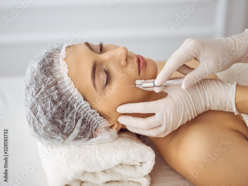 Beautician doing beauty procedure with syringe to face of young brunette woman. Cosmetic medicine and surgery, beauty injections