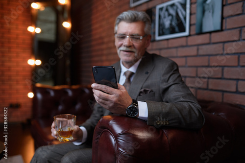A successful Mature Director holds an online conference and drinks whiskey in his office.
