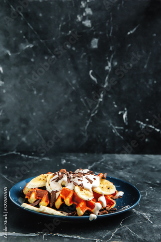 Viennese waffles on a plate, with a crumb of chocolate and slices of banana on a dark textured background.
