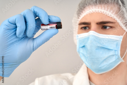 Doctor in protective coverall and face mask holding blood sample in hand