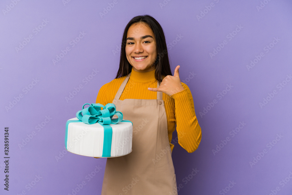 Young asian woman holding a cake isolated showing a mobile phone call gesture with fingers. Young asian woman holding a cake isolated showing a mobile phone call gesture with fingers.