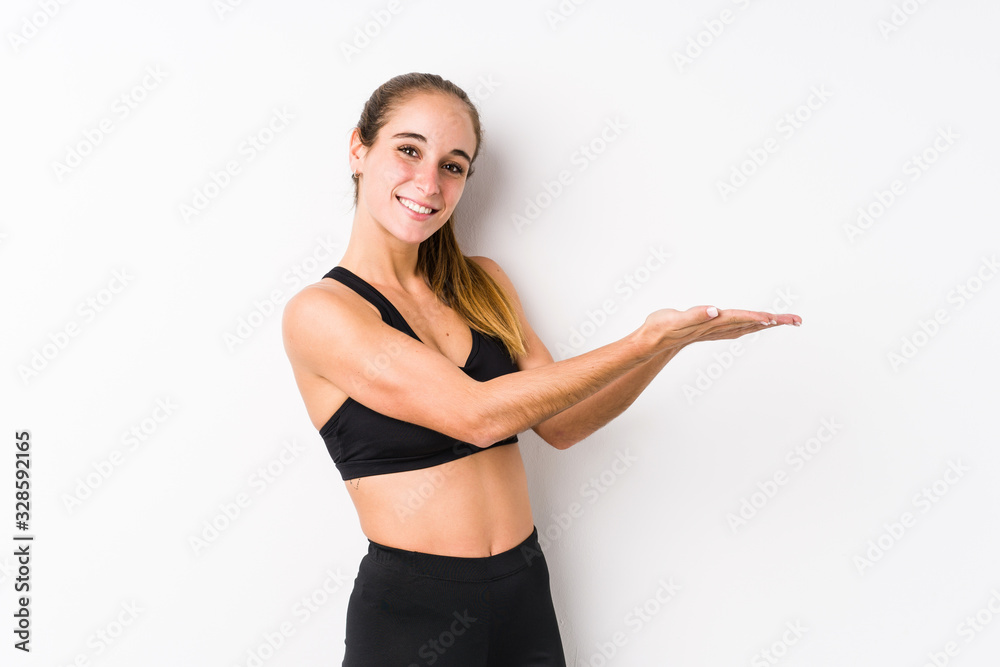 Young caucasian fitness woman posing in a white background holding a copy space on a palm. Young caucasian fitness woman posing in a white background holding a copy space on a palm.