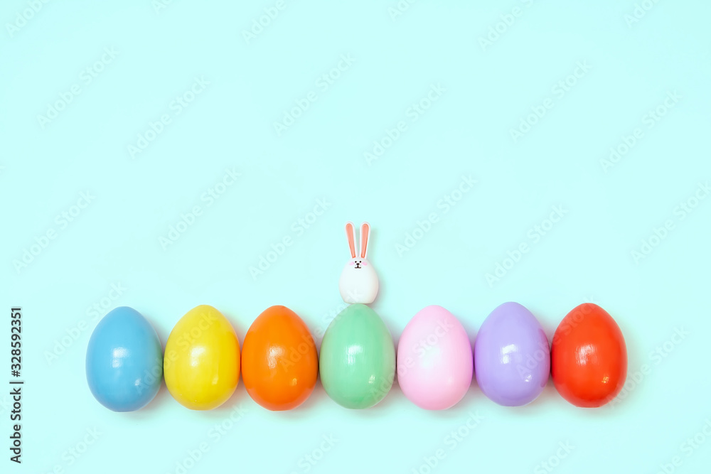 Top view of an Easter composition of painted eggs in bright juicy colors on a blue background with a little rabbit. Holiday concept, flat layout, minimalism