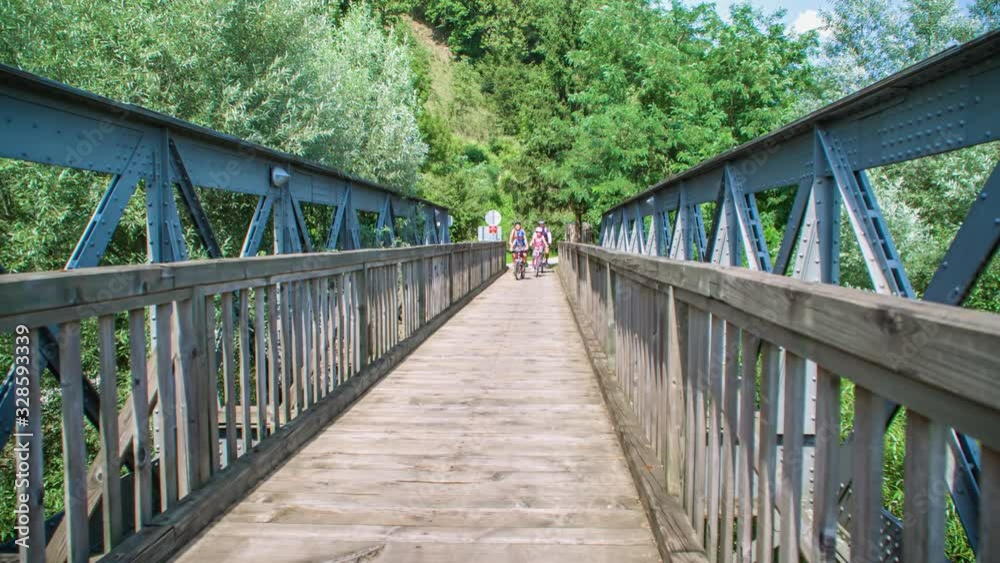 Slow motion of a family riding bikes across a wooden footbridge towards the camera Slow motion of a family riding bikes across a wooden footbridge towards the camera