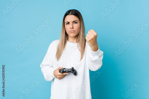 Young caucasian woman holding a game controller showing fist to camera, aggressive facial expression.