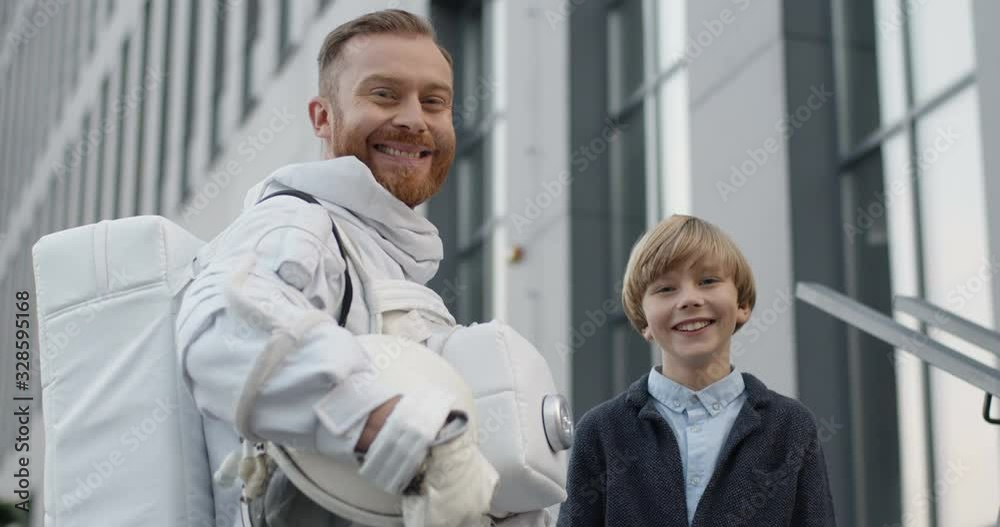 Portrait of little cute Caucasian boy with spaceman in armor smiling cheerfully together to camera. Teen small son and father cosmonaut who coming back home from cosmos. Outdoors. Portrait of little cute Caucasian boy with spaceman in armor smiling cheerfully together to camera. Teen small son and father cosmonaut who coming back home from cosmos. Outdoors.