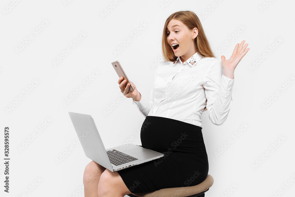 Image of a young pregnant businesswoman wearing glasses, a girl holding a smartphone looking at the screen, and holding a laptop sitting on a chair
