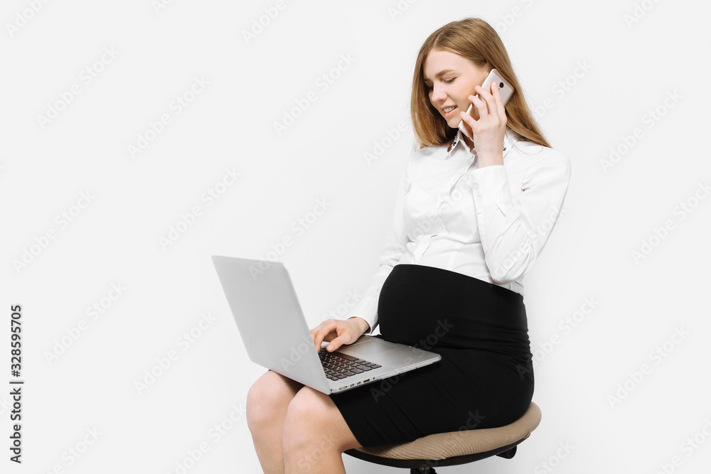 Image of a young pregnant businesswoman in glasses, a girl talking on the phone and working with a laptop, sitting on a chair Image of a young pregnant businesswoman in glasses, a girl talking on the phone and working with a laptop, sitting on a chair