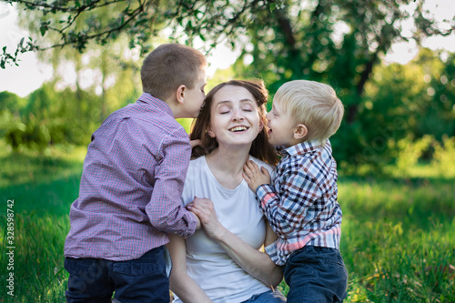 Little sons kiss mom on the cheek. Happy mother with two children in nature.