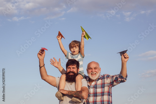 Happy smiling boy on shoulder dad looking at camera. Happy family. Child pilot aviator with paper airplane dreams of traveling. Generation concept.