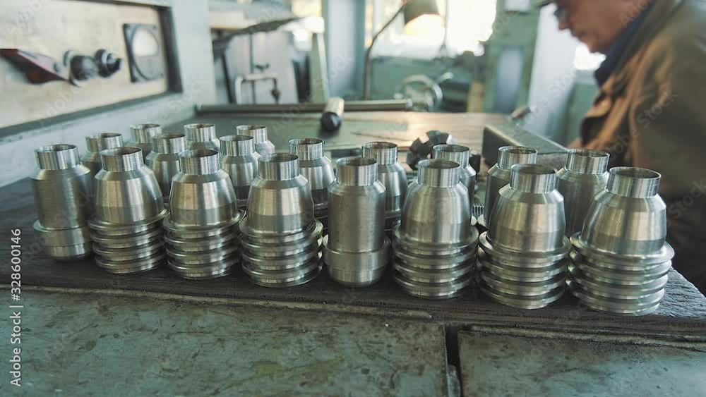 A professional factory worker in gloves interacts with a group of technological metal parts.