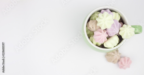 Marshmallow multicolored. Meringue marshmallows in a green cup on a light background. Colorful meringues on a white background. Lots of sweet marshmallows. Banner. copyspace