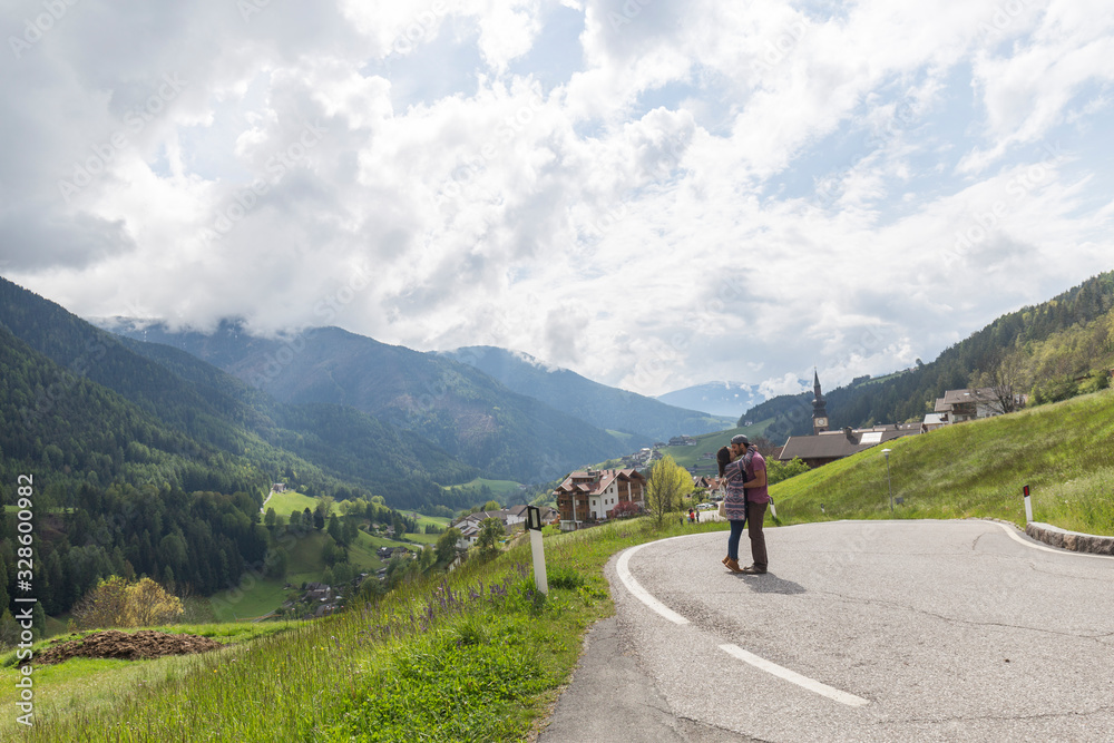 couple kisses in the middle of the road in a rural village of the italian alps cloudy day, vegetation abounds