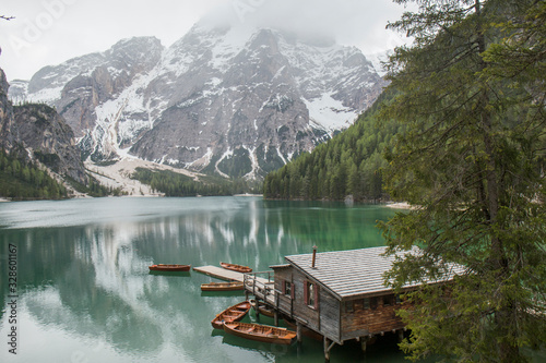 landscape of Lago di Braies, impressive green lake, which reflects the high snowy mountains, surrounded by abundant green vegetation, we can also see a wooden cabin that is the jetty and some wooden b