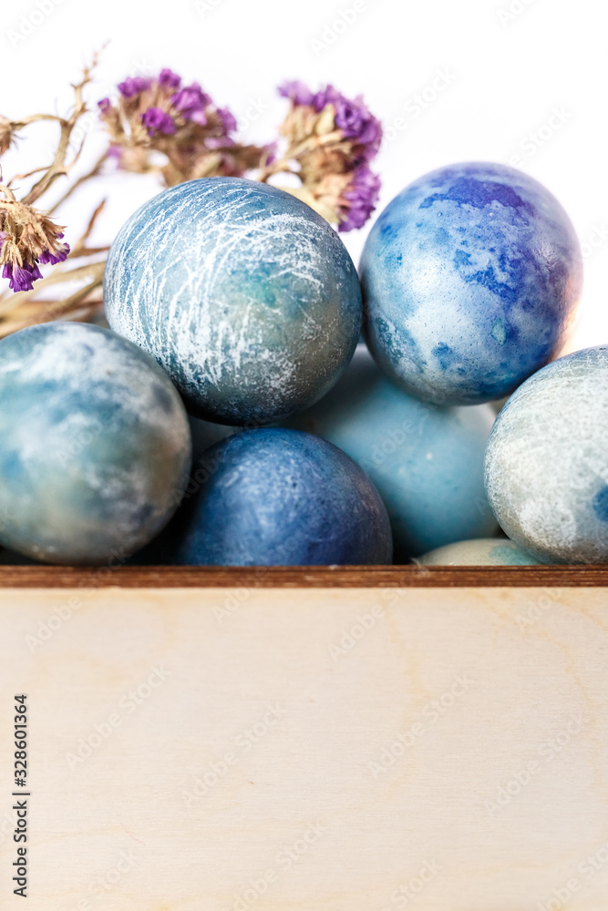 Easter colored eggs in a wooden box on white background. Easter eggs and spring flowers. Holiday pattern.