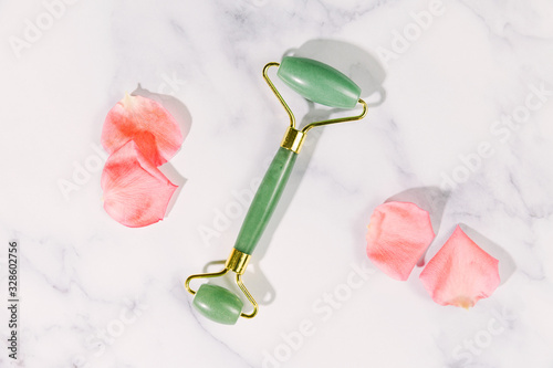 Fototapeta Naklejka Na Ścianę i Meble -  Jade roller and pink rose petals / still life on white marble background / Wellness and self love concept