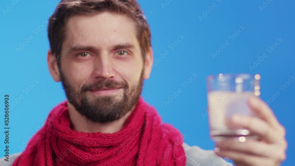 Young handsome man in red scarf holds glass of watter pouring soluble pill dissolving drinking treatment of cold feel much better smile happy at camera. On background. Healthcare, medication.
