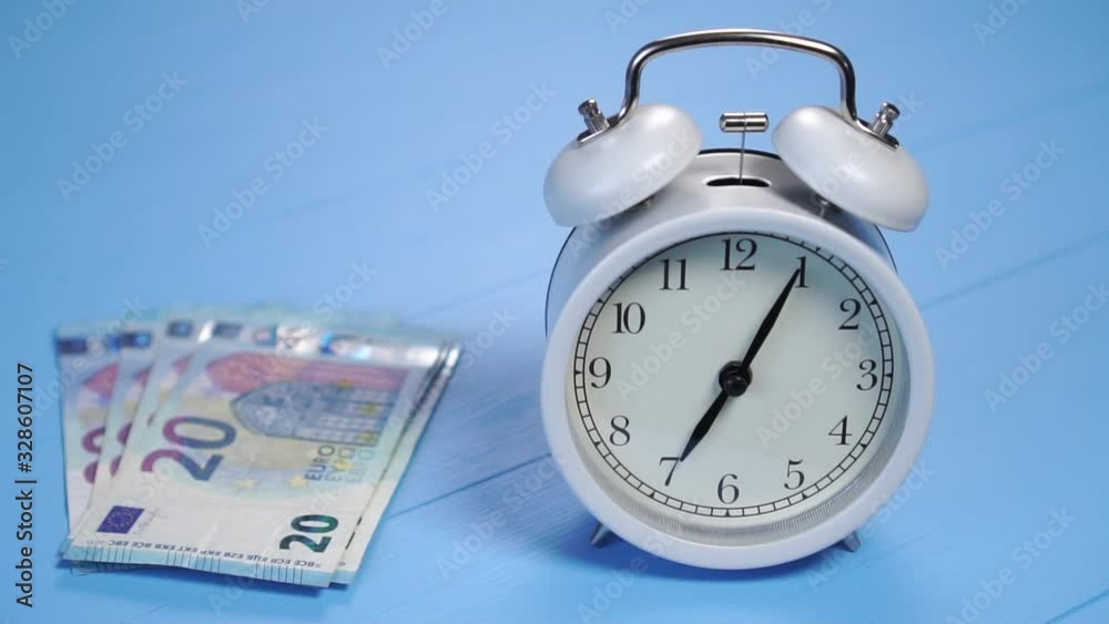 A bundle of twenty euro banknotes falls next to an analog gray clock on a blue wooden table with texture. Slow motion close up. The concept of profitable investment of money and payment of taxes A bundle of twenty euro banknotes falls next to an analog gray clock on a blue wooden table with texture. Slow motion close up. The concept of profitable investment of money and payment of taxes