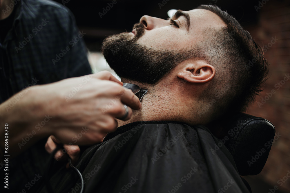 Obraz premium Good looking young adult man getting a hair and beard styling and dressing treatment by professional hairstylist.