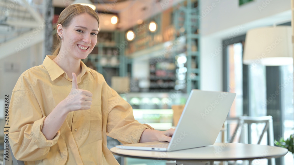 Thumbs up by Young Woman using Laptop in Cafe Thumbs up by Young Woman using Laptop in Cafe