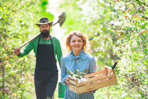 Young couple in spring orchard looking into the camera. Small business owner selling organic fruits and vegetables. Portrait of pair of farms Working In Garden Together.