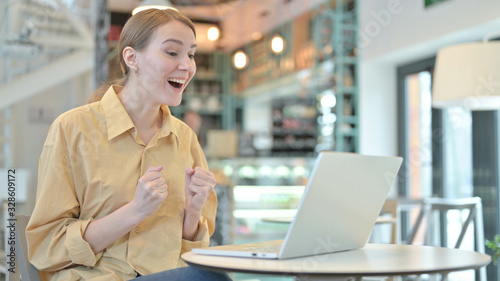 Young Woman Celebrating Success on Laptop in Cafe