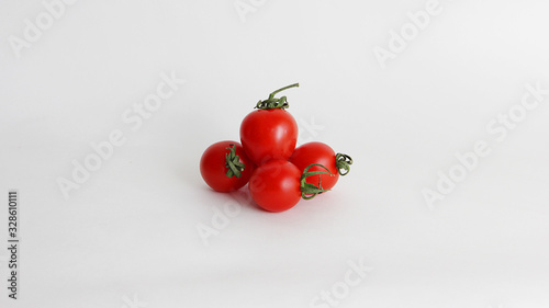 small red cherry tomatoes with green tails lie scattered on a white background © kristinatodoreva
