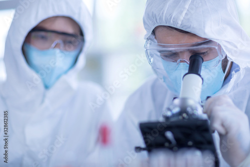 A male scientist wearing a mask and looking through the microscope in the laboratory, Concept, The scientists wear white protective clothing is experimenting with drug anti- Coronavirus, Covid2019 photo