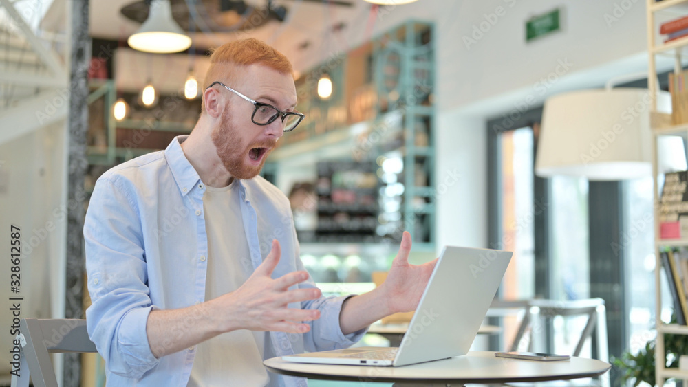 Redhead Man Celebrating Success on Laptop in Cafe