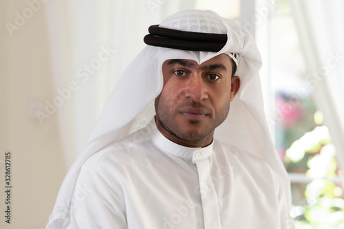 Closeup head shot of handsome Emirati man wearing traditional kandura or thobe  & ghutra looking at camera
