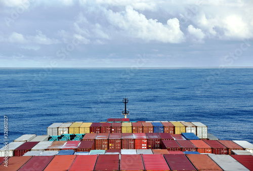 Close up view on the containers loaded on deck of the large cargo ship. She is sailing through calm, blue ocean. 