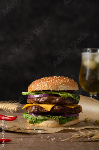 Homemade burger with grilled beef cutlet, sauce, vegetables and a glass of beer in the background. Copy space.