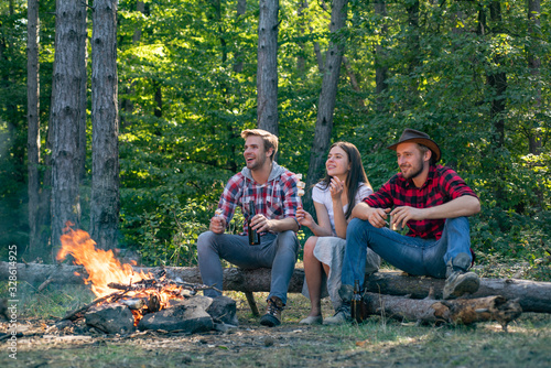Happy young friends having picnic in the country. Company adult friends relaxing near campfire. Young couples having picnic in woods. Young people enjoying picnic in park on summer day.