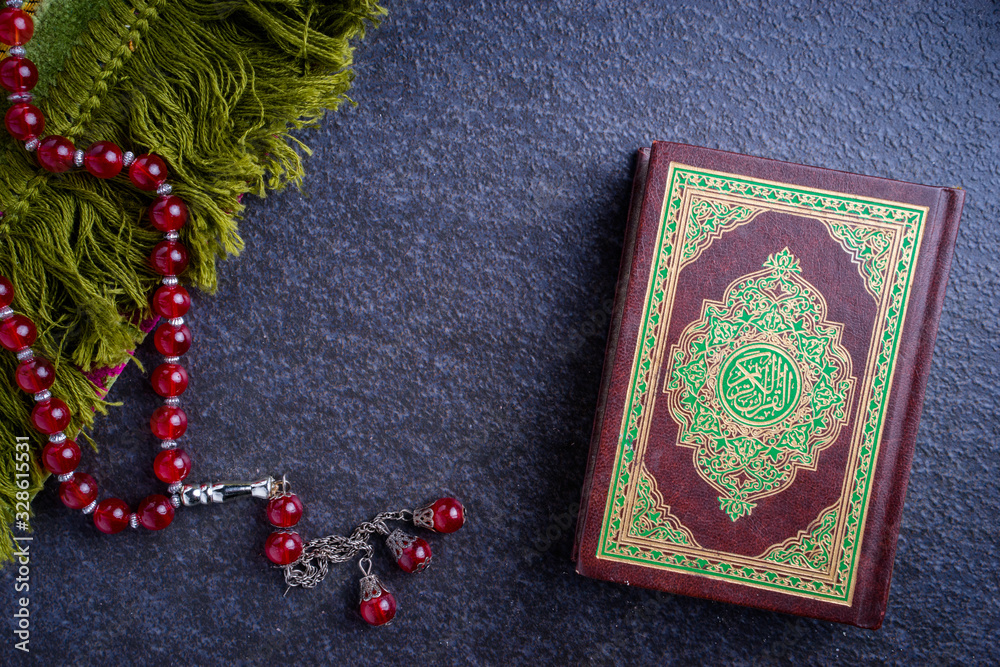 Eid Mubarak or Islamic concept. The Islamic holy book, Quran or Kuran, with rosary beads or “tasbih” on grey background. Arabic words on the book means Eid Mubarak or Islamic concept. The Islamic holy book, Quran or Kuran, with rosary beads or “tasbih” on grey background. Arabic words on the book means