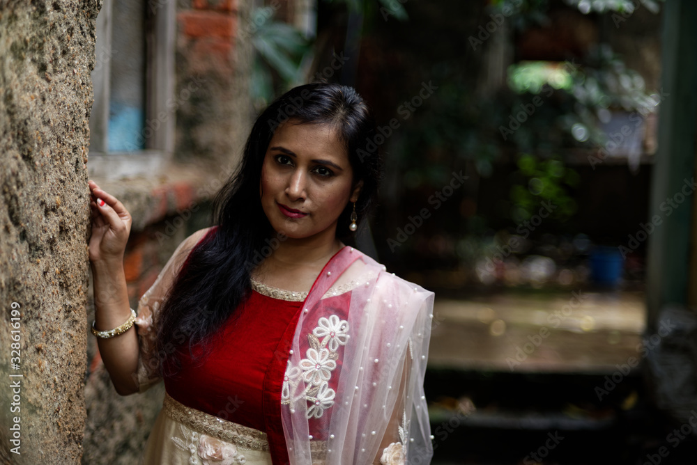 Portrait of an young and attractive Indian Bengali brunette woman standing in front of a vintage brick wall wearing Indian traditional ethnic cloths. Indian lifestyle and fashion