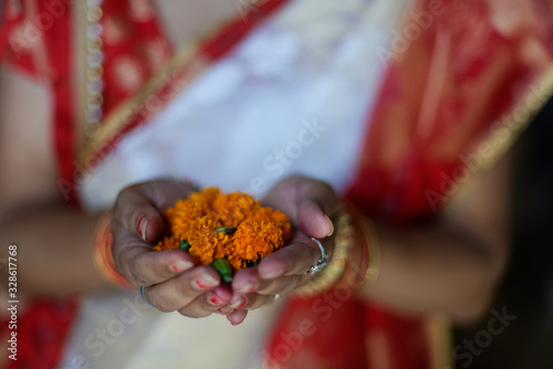 An Indian Bengali lady in bengali ethnic and traditional dress offering orange flowers as homage holding in her palms. Indian culture and lifestyle.