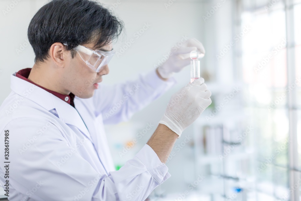A male Asian scientist wearing a white robe and looking at a glass tube Is a research about medicine in the laboratory. Concept, The scientist with drug anti- Coronavirus or Covid2019. A male Asian scientist wearing a white robe and looking at a glass tube Is a research about medicine in the laboratory. Concept, The scientist with drug anti- Coronavirus or Covid2019.