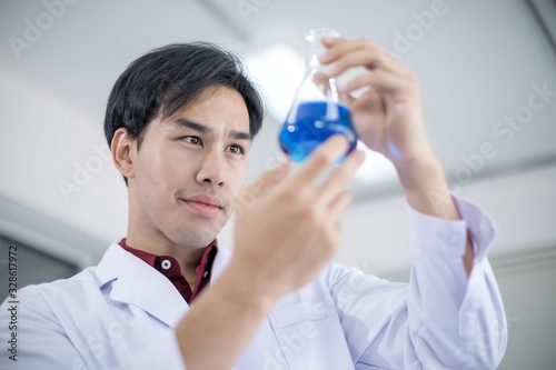A male Asian scientist wearing a white robe and looking at a glass tube Is a research about medicine in the laboratory. Concept  The scientist  with drug anti- Coronavirus or Covid2019.
