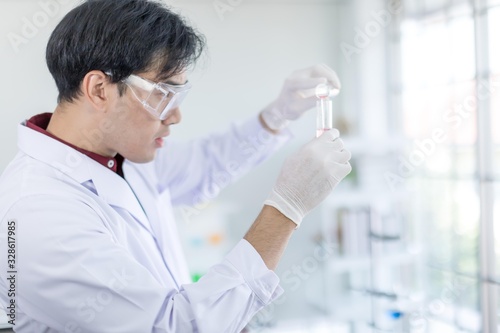A male Asian scientist wearing a white robe and looking at a glass tube Is a research about medicine in the laboratory. Concept  The scientist  with drug anti- Coronavirus or Covid2019.