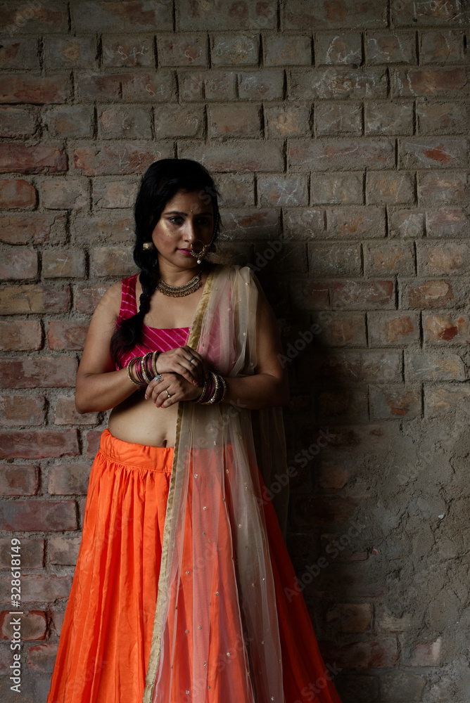 Portrait of an Young and beautiful Indian Bengali brunette woman standing in front of a vintage brick wall wearing Indian traditional ethnic vibrant skirt blouse. Indian lifestyle and fashion