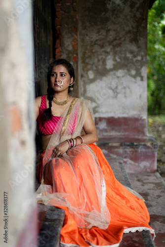 Portrait of an Young and beautiful Indian Bengali brunette woman sitting on the staircase of a vintage house wearing Indian traditional ethnic vibrant skirt blouse. Indian lifestyle and fashion