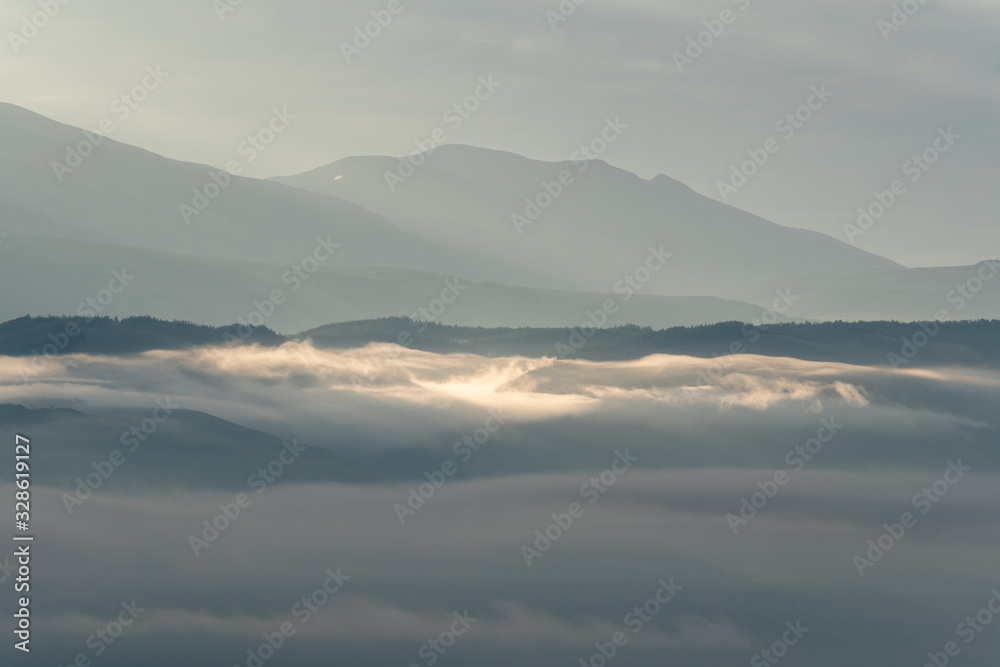 clouds and rays of dawn in mountain valley, soft light in early morning, meditation in nature. Gentle hills in bluish haze, silhouettes of mountains clouds and rays of dawn in mountain valley, soft light in early morning, meditation in nature. Gentle hills in bluish haze, silhouettes of mountains