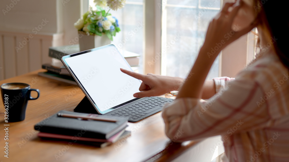 Fototapeta premium Widok z boku dziewczyny college'u dzwoniącego podczas pracy nad swoim zadaniem z makietą tabletu i papeterii
