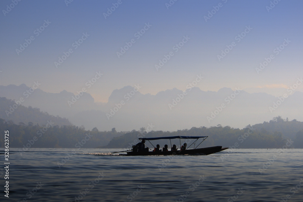 Silhouette long tail boat with passenger on board. ship adventure in to lake and river in a forest wetland. soft morning sky and mountains outlined Silhouette long tail boat with passenger on board. ship adventure in to lake and river in a forest wetland. soft morning sky and mountains outlined