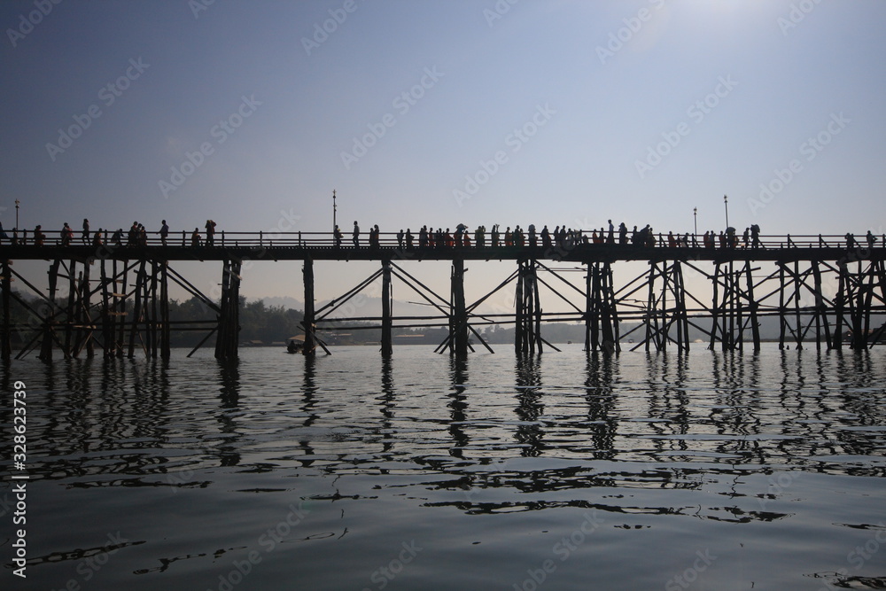 Silhouette Mon bridge during red sunset scene, traditional wooden construction crossing the Song river Sangkhlaburi, Thailand. Travel destination landmark. bridge cutting across mountain and lake.