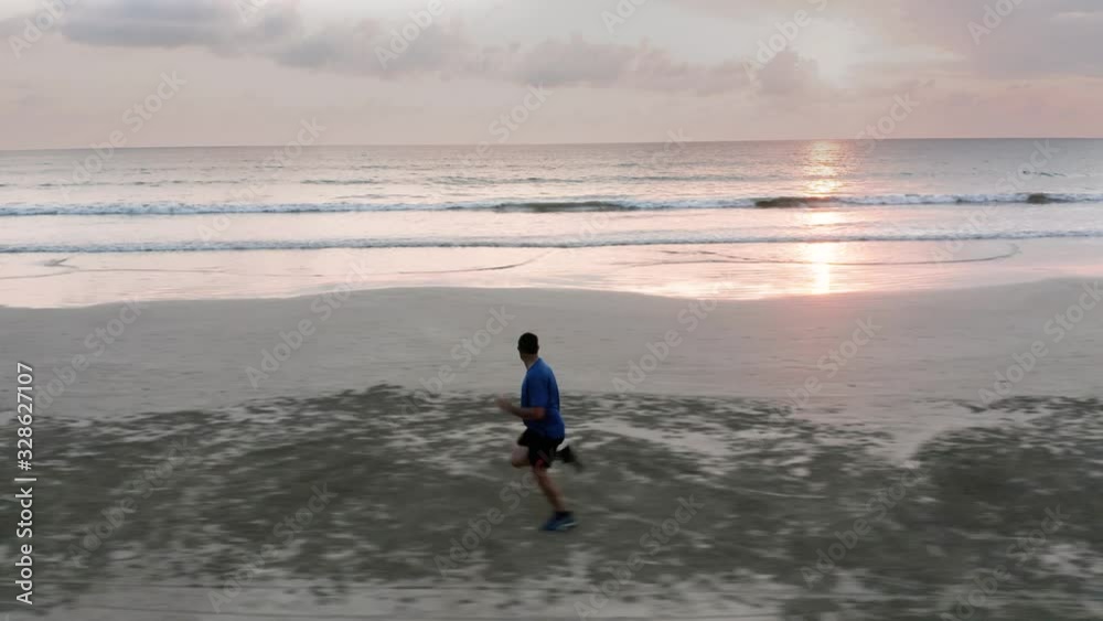 A male runner on a tropical beach with a background sunset over the ocean A male runner on a tropical beach with a background sunset over the ocean